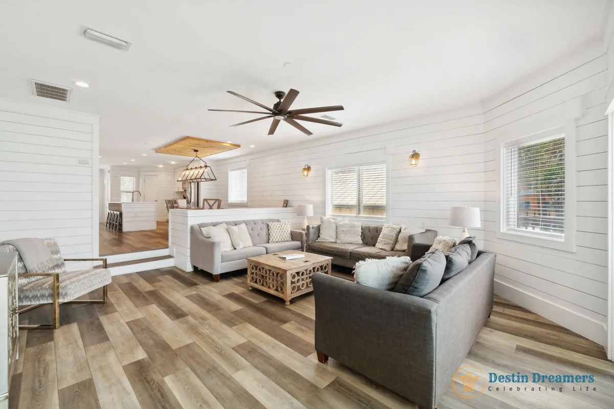 A welcoming entertainment area featuring a large sectional sofa, stylish light fixtures, a ceiling fan, and a wooden coffee table. The arrangement is ideal for both intimate and group gatherings, offering ample space for relaxing, reading, or hosting lively game or movie nights.
